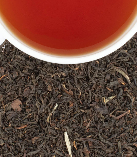 Cup of Earl Grey Supreme tea with loose black tea leaves background