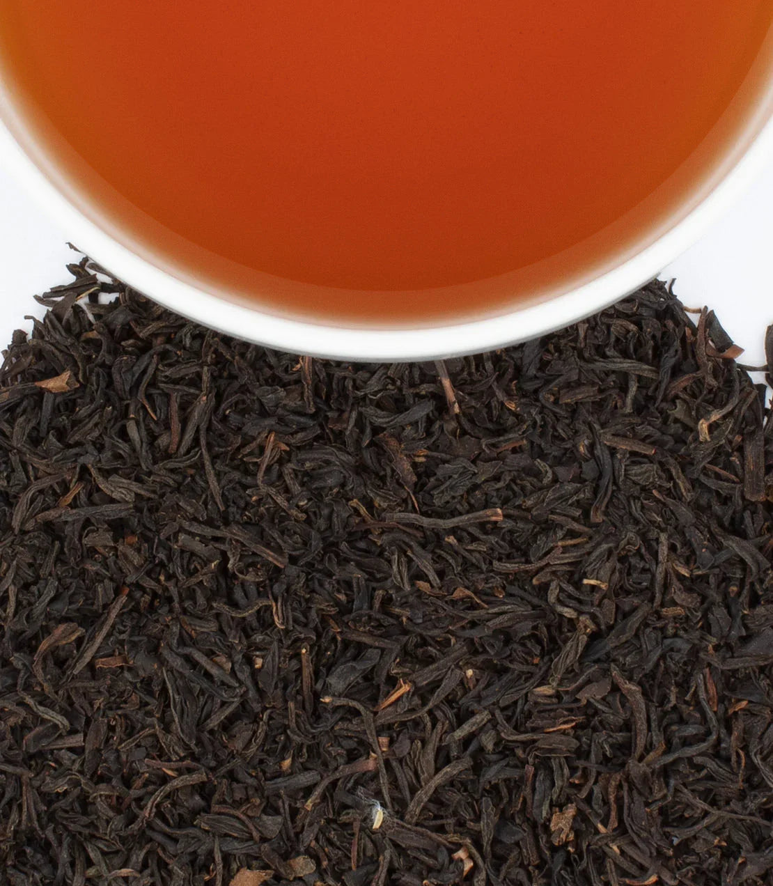 English Breakfast tea in white cup with loose black tea leaves on white background