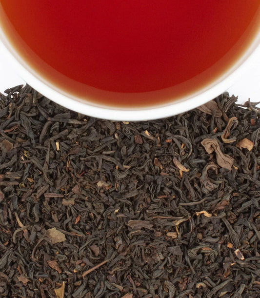 Earl Grey tea in white cup above loose black tea leaves on white background