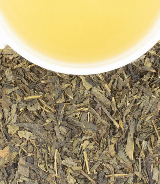 Cup of cherry blossom green tea with loose leaf tea on white background