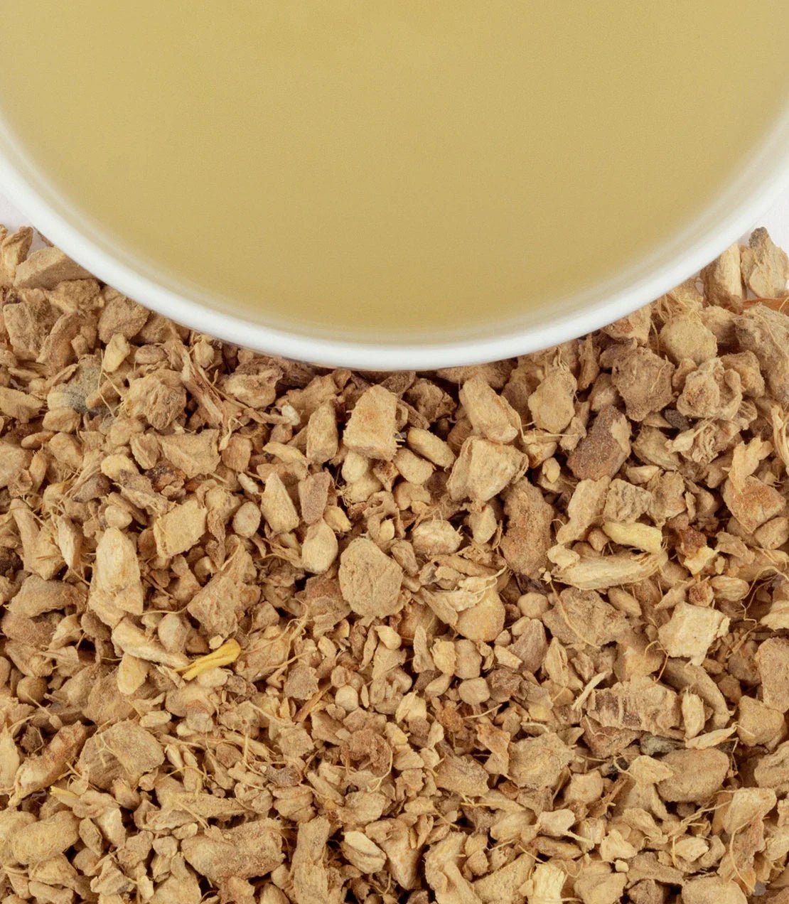Cup of ginger tea with loose dried ginger pieces on a flat surface