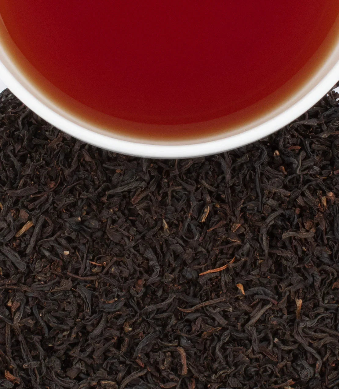 Cup of English Breakfast tea on loose black tea leaves, close-up top view