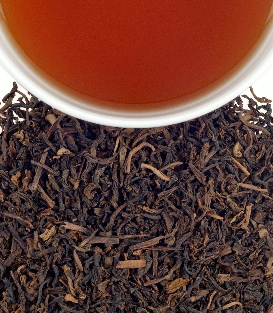 Close-up of vanilla black tea leaves with a cup of brewed Vanilla Comoro tea