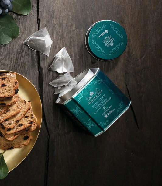 Earl Grey Imperial tea tin with sachets and sliced biscotti on wooden table