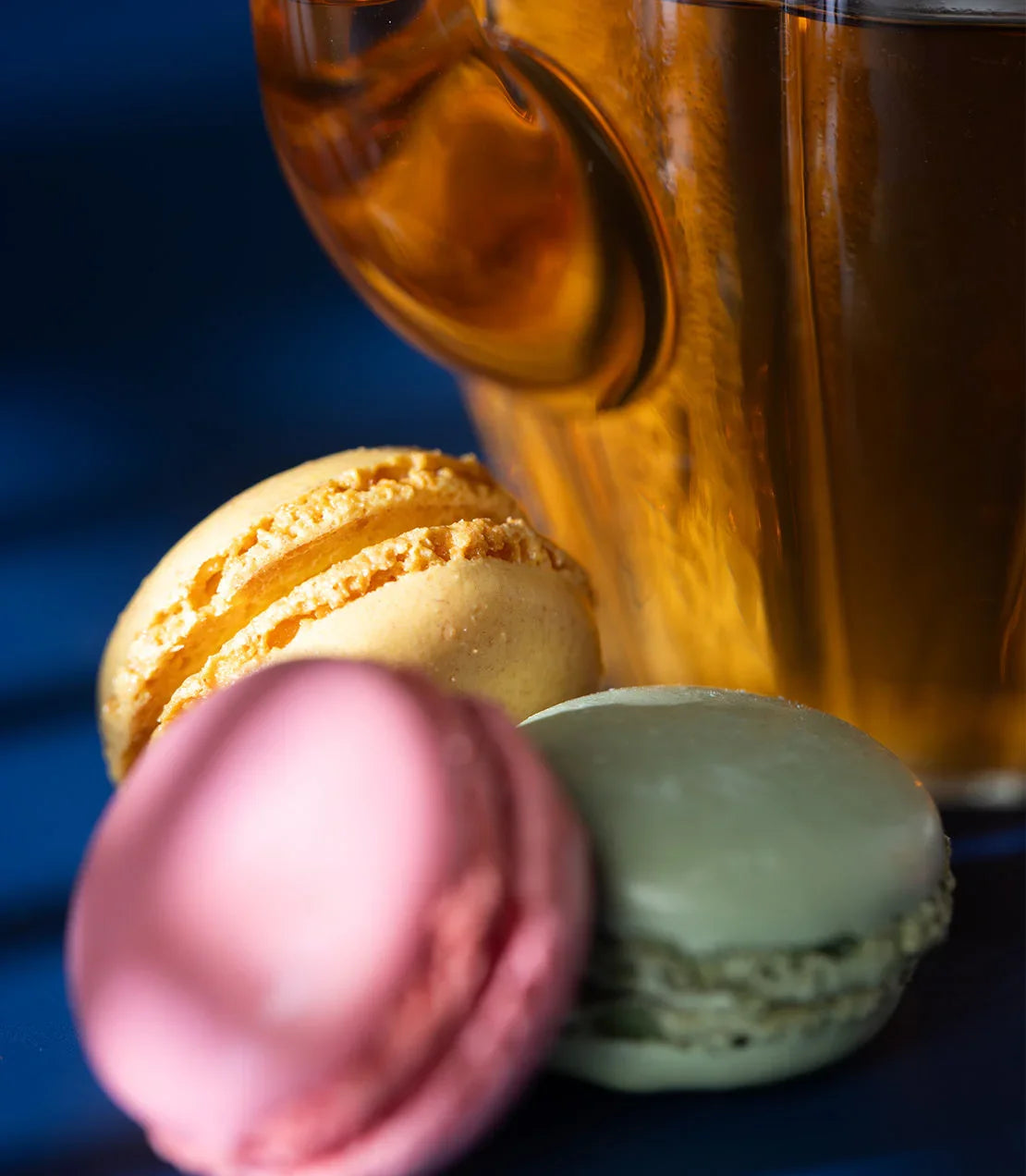 Colorful French macarons with a glass cup of tea on a blue surface