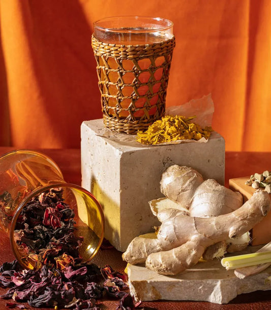Glass of herbal tea with woven cover, fresh ginger, turmeric, dried hibiscus on rustic blocks