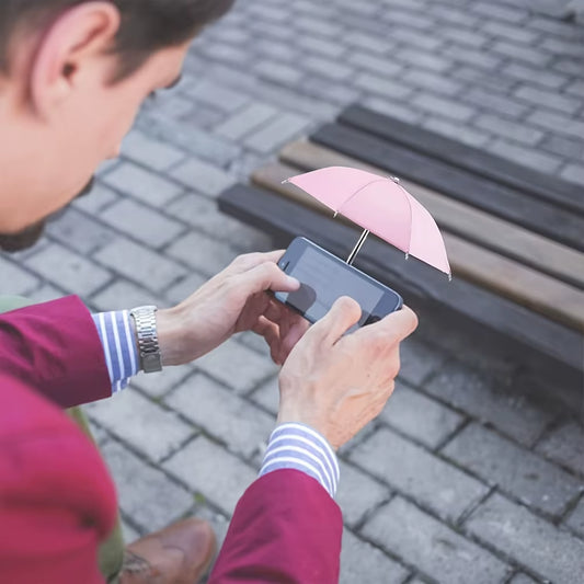 Man using phone outdoors with small pink umbrella accessory for smartphone on bench