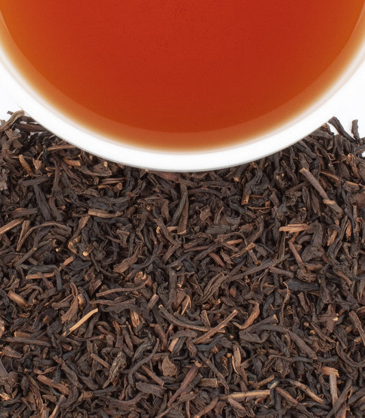 Cup of brewed decaf tea with loose leaf black tea on white background