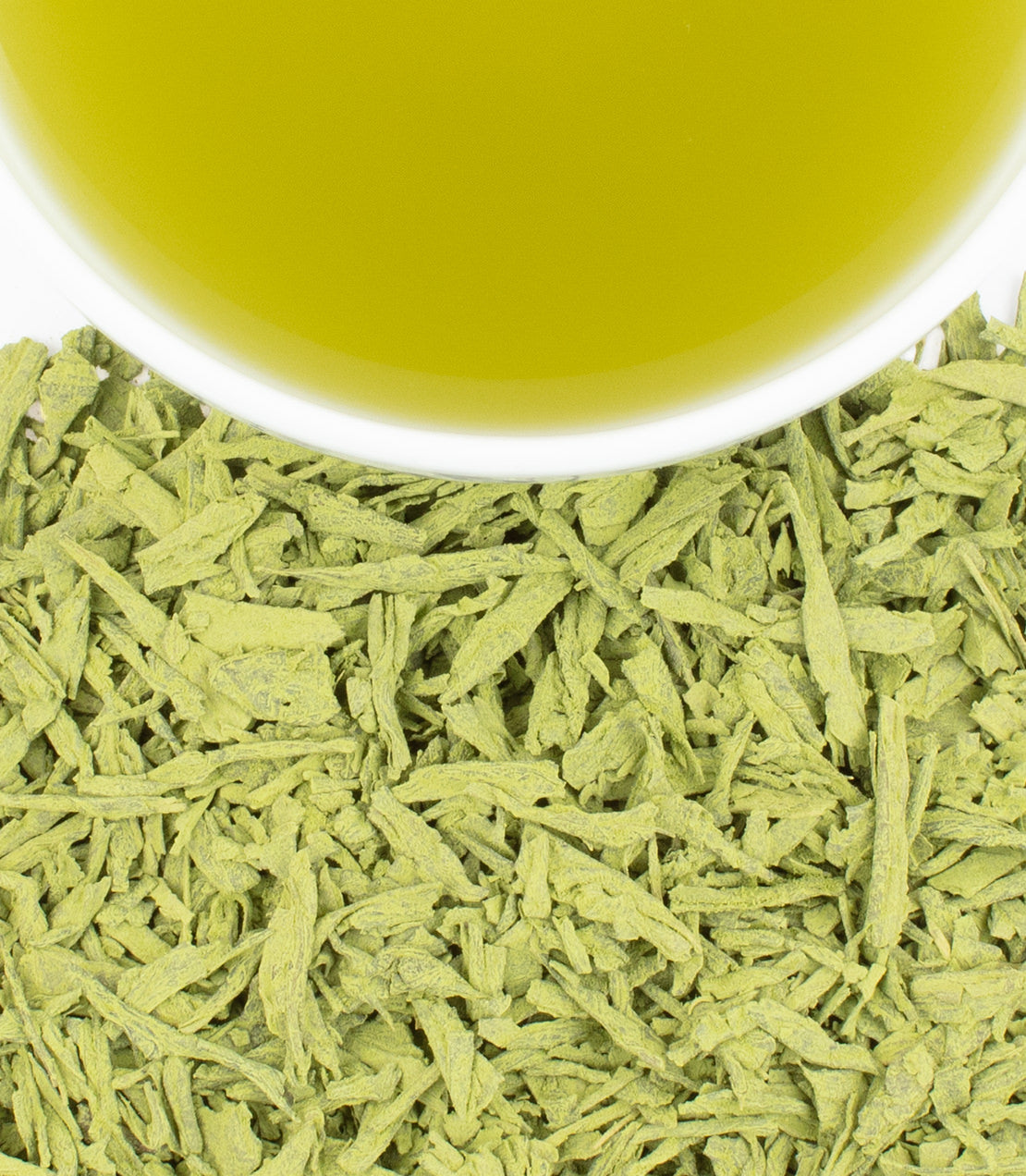 Close-up of green tea leaves with a cup of tea in the background