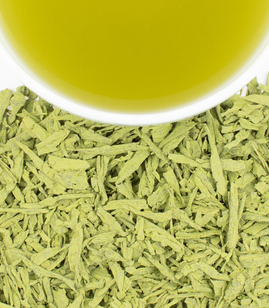 Close-up of green tea leaves with a cup of tea in the background