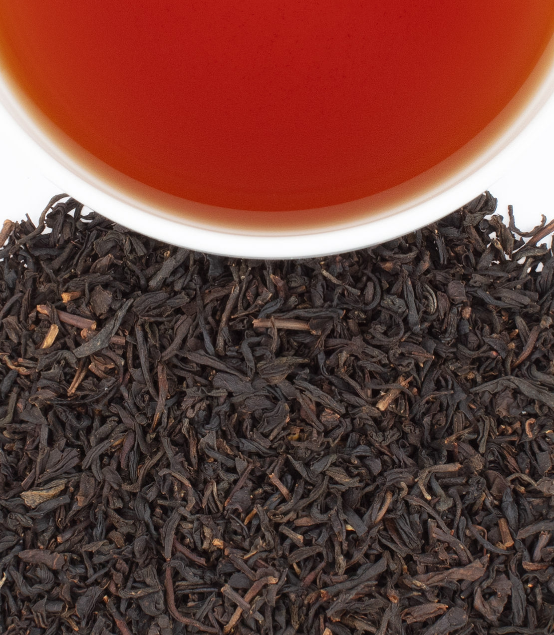 Close-up of black tea leaves with a cup of tea in the background