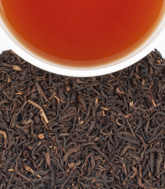 Close-up of chai tea leaves with a cup of tea in the background