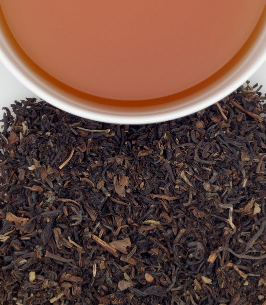Close-up of darjeeling tea leaves with a cup of tea in the background - blinks emporium