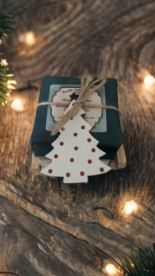 Handmade soap gift set wrapped with twine and a wooden Christmas tree tag on rustic wood