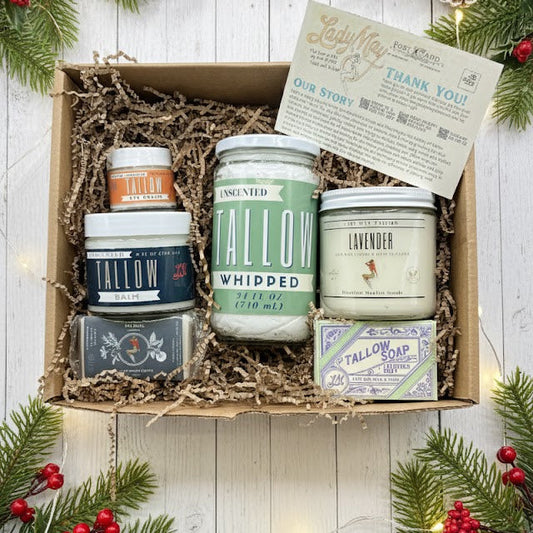 Gift box with assorted tallow skincare products on wood, surrounded by festive greenery.